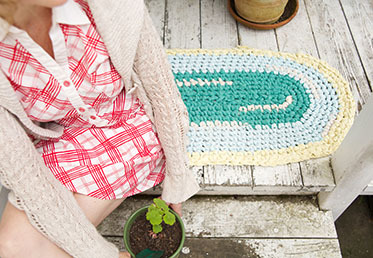 A person sitting on a green, teal, and cream-colored rug laid on a whitewashed wooden porch.