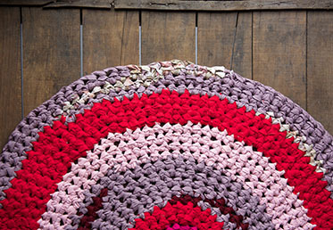 A pink, purple, and red crocheted rug on a wooden floor.