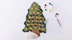 A felt tree with numbered pockets containing small paint tubes, beside a paint palette and paintbrush, made by Kata Golda in her Felt Advent Calendar class on Creativebug.