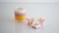 A striped handmade candle next to three tiny handmade candles in heart, star, and diamond shapes.