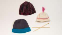Three knit hats and a pair of knitting needles.