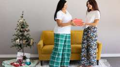 A mother and daughter holding a wrapped present between them, wearing hand-sewn pajama pants in green plaid and dark floral.