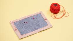 An open handmade needle book laced with pins and needles alongside a ball of bright red DMC pearl cotton thread.