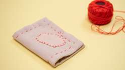 A closed handmade needle book next to a ball of bright red DMC pearl cotton thread.