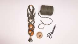 An overhead image of a string-bag holding onions, a spool of jersey yarn, a spool of twine, and a pair of scissors.