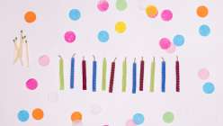 A row of multi-colored handmade beeswax candles on a table strewn with paper polka-dots.
