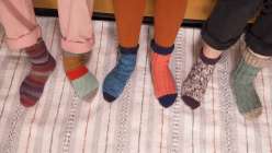 the pairs of colorful handmade socks on three pairs of feet on the rug