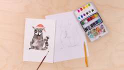 A pencil sketch of a raccoon wearing a Santa hat eating a candy cone, next to the same raccoon painted in watercolor, both from Maria Carluccio's Celebrate the Season Daily Holiday Painting Practice class on Creativebug.