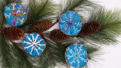 Three hand-embroidered snowflake ornaments on the background of an overground bough with pinecones from the Rebecca Ringquist Embroidered Snowflake Ornament class on Creativebug.