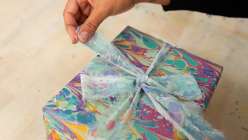 Hand tying a marbled ribbon around a package wrapped in hand-marbled paper