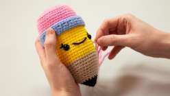 A pair of hands holding a crocheted pencil stuffy from Vincent Green-Hite's Amigurumi Techniques: Change Colors in the Round Creativebug class
