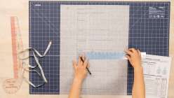 An overhead image of a pair of hands holding a ruler and drafting measurements onto a piece of paper from Sanae Ishida's Draft and Sew a Torso Sloper and Muslin class on Creativebug