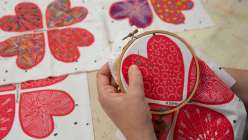 A hand holding an embroidery hoop stretched with heart-printed fabric from Rebecca Ringquist's Embroidered Heart Ornaments Creativebug class