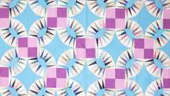 An image of Sarah Bond's Pickle Wedges quilt stitched in purples, blues, whites and patterned cotton fabrics.