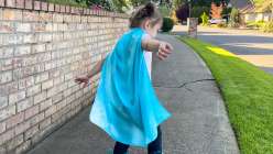 A toddler wearing a teal silk play cape from the Easy Dyed Silk Play Cape class by Melissa Lang Lytle on Creativebug