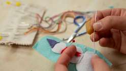 A pair of hands stitching a felt appliqué of a snowman from Rebecca Ringquist's 12 Days of Christmas: Sew an Heirloom Stocking class on Creativebug