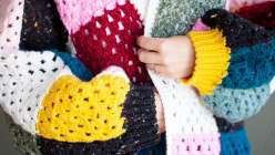 Twinkie Chan wearing a multicolored crochet sweater with yellow ribbed cuffs she made in her Crochet a Granny Square Cardigan class on Creativebug. 