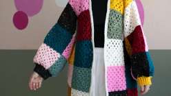 Twinkie Chan wearing a multicolored crochet sweater with yellow ribbed cuffs that she made in her Crochet a Granny Square Cardigan class on Creativebug. 