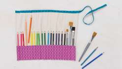 A purple pencil roll full of a rainbow of colored pencils, made in Faith Hale's Sew a Paint Brush and Pencil Roll class on Creativebug.