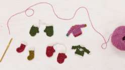 A pair of tiny crocheted mittens, a pair of crocheted stockings, and two tiny crocheted sweaters made by Twinkie Chan in her Holiday Crochet Applique class on Creativebug