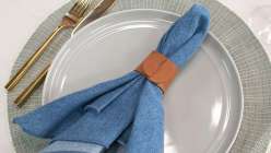 A blue napkin with a tan leather napkin ring made in the Make Leather Napkin Rings class on Creativebug