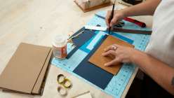 A pair of hands cutting book board from Cobrina's Make an Upcycled Flower Press class on Creativebug.