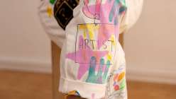A colorful white jumpsuit embellished with tassels, hand-carved stamps, embroidery, painting, and drawings, made by Risa Iwisaki Culbertson in her class Wearable Wins on Creativebug