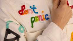 A white jumpsuit with rainbow-colored embroidery reading 