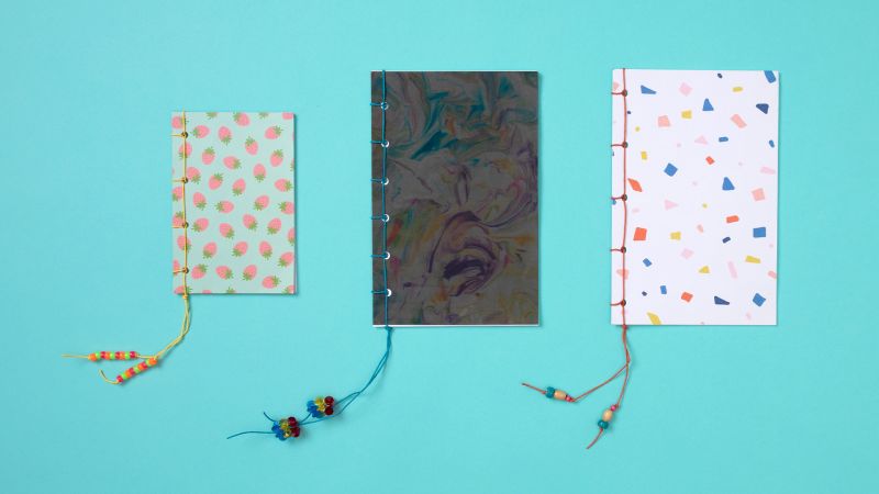 Three Japanese side sewn paper books with decorative beading on a teal background 