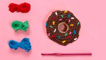 crocheted donut with yarn and crochet hook on pink background